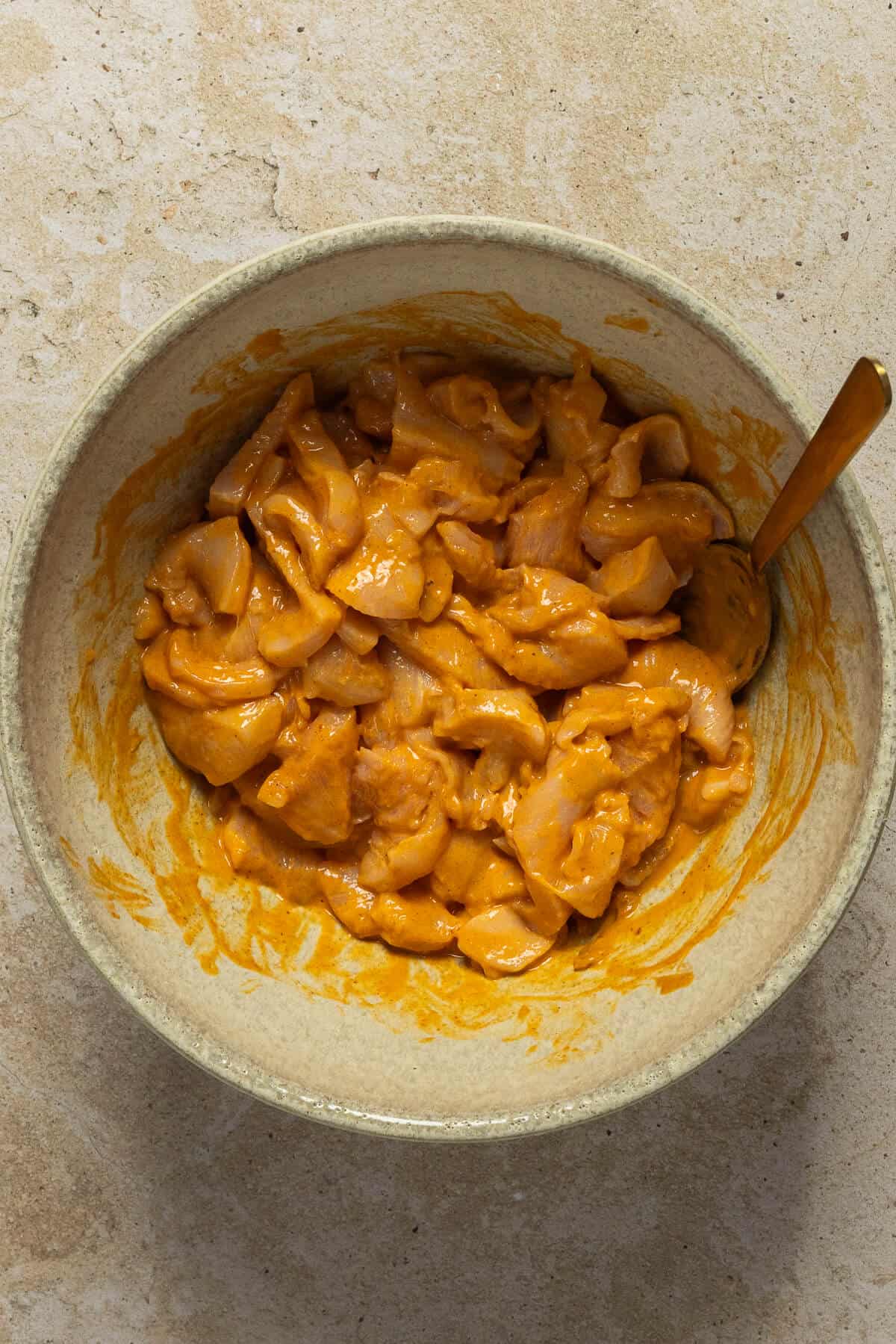 A large mixing bowl with the raw chicken tossed in the satay marinade.