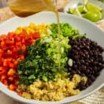 A large mixing bowl of cowboy caviar with quinoa with dressing being poured over the top.