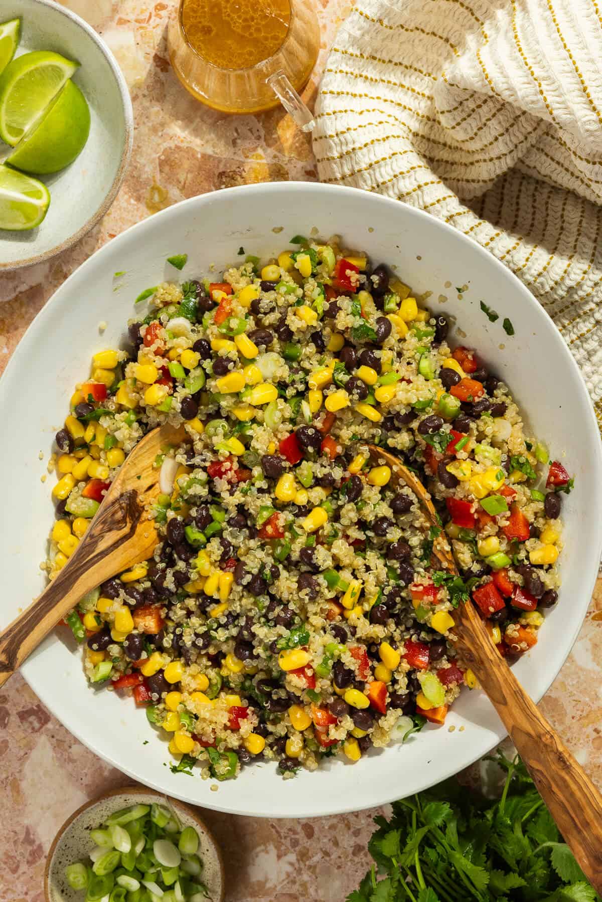 A large mixing bowl of cowboy caviar with quinoa tossed with two wooden spoons.