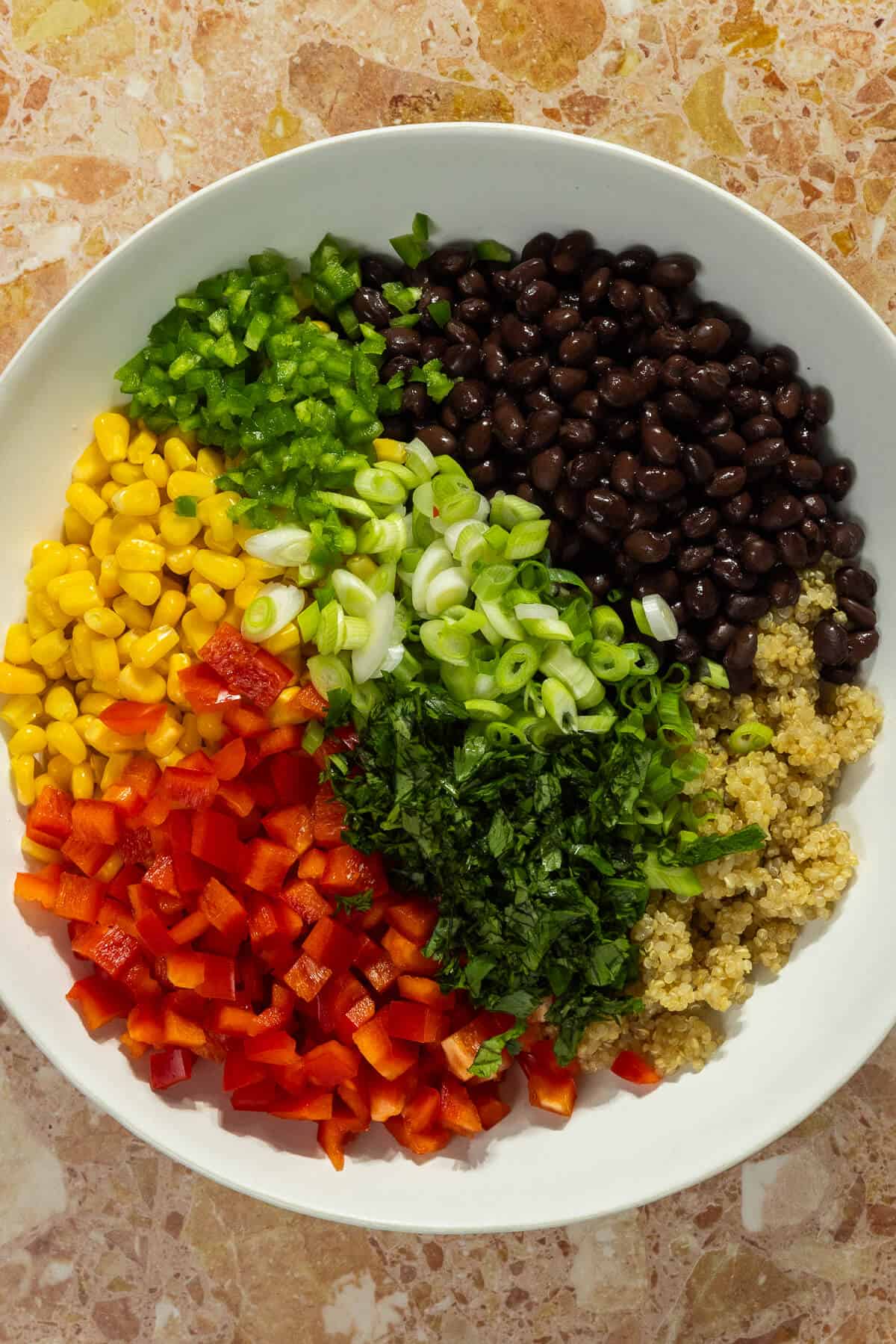 A large mixing bowl of cowboy caviar with quinoa prior to being mixed.