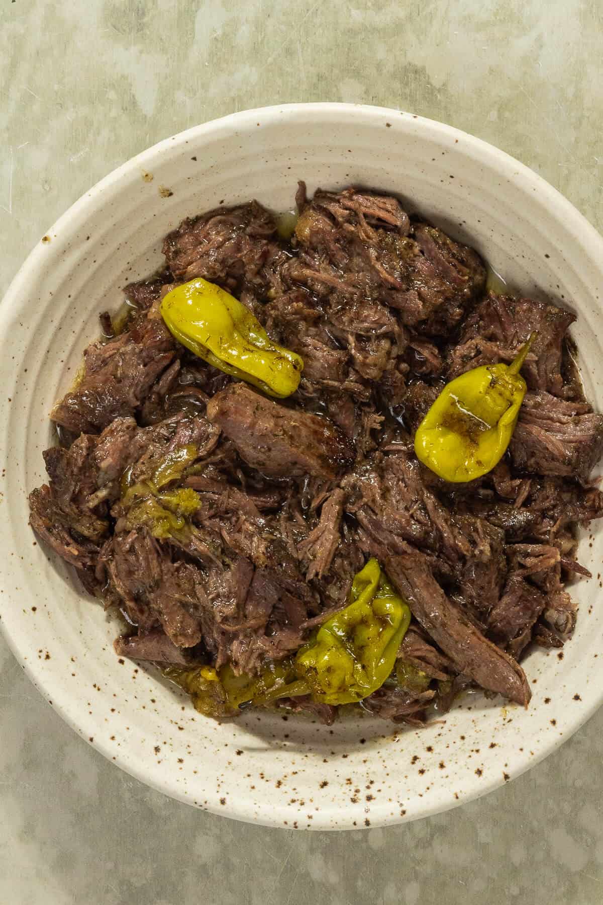 A bowl of Mississippi pot roast with pepperoncini peppers on top.