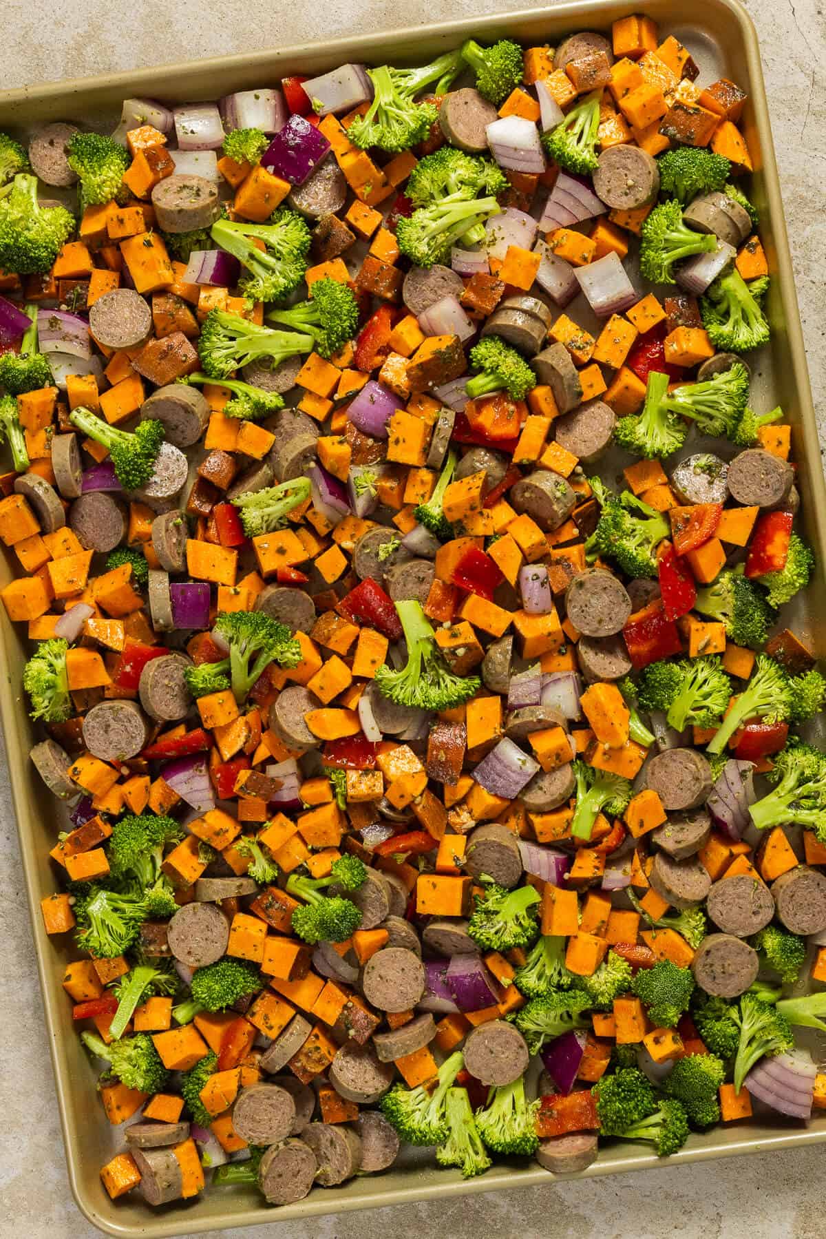 A sheet pan with the pesto chicken sausage and veggies prior to roasting.