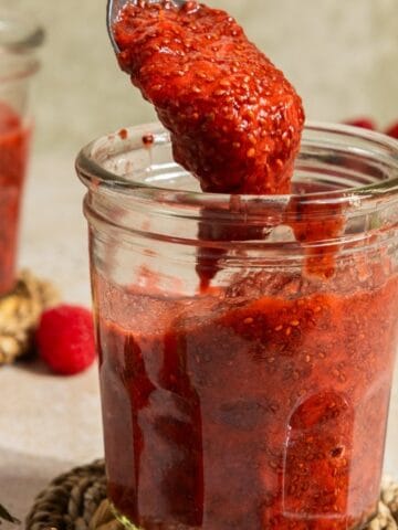 Fresh strawberry jam being spooned into a glass jar for storage.