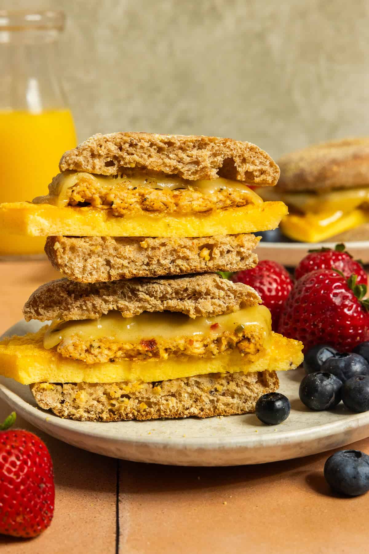 Two sausage breakfast sandwiches stacked on a plate with berries.