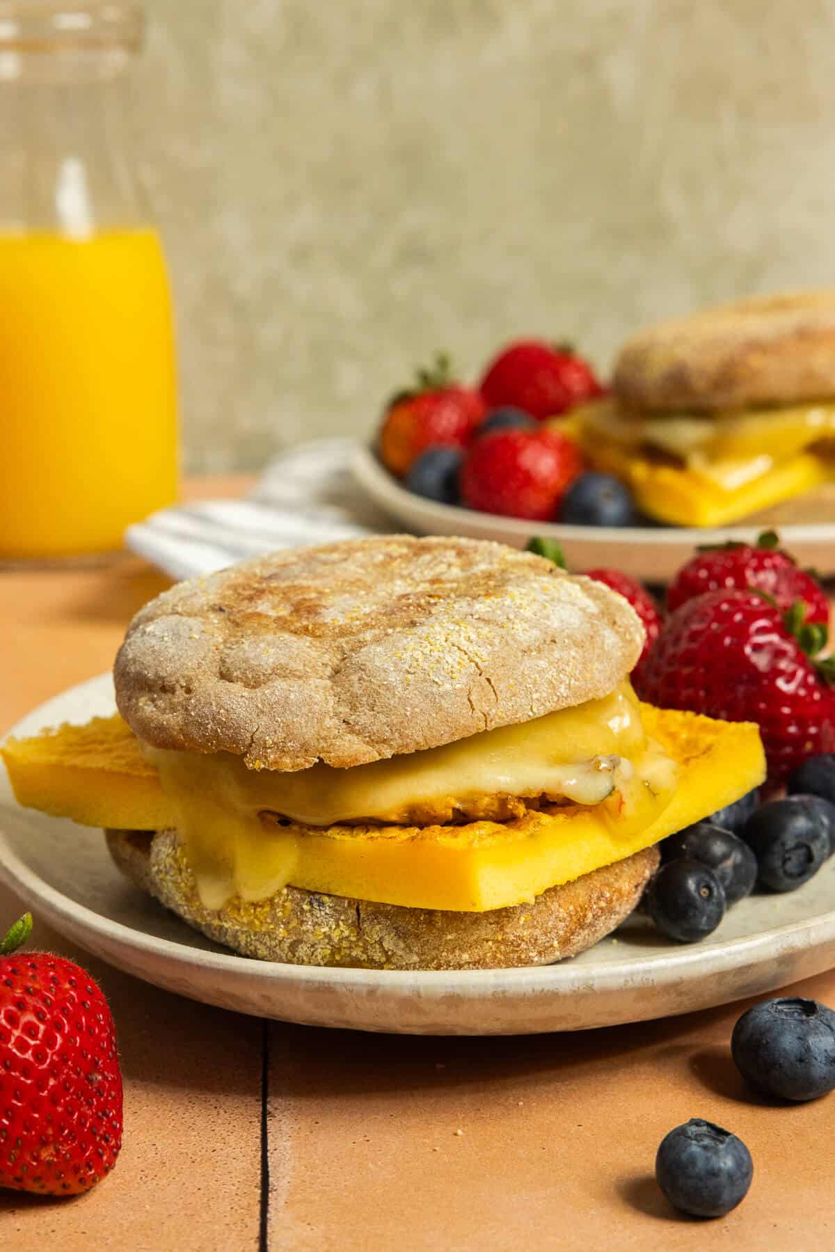 A plate with a sausage breakfast sandwich and berries.