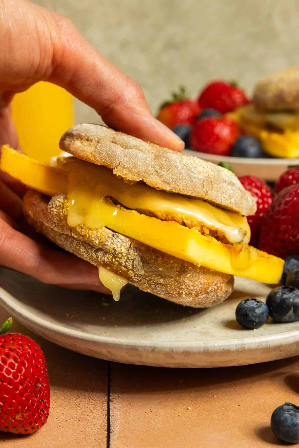 A hand holding a chicken sausage breakfast sandwich.