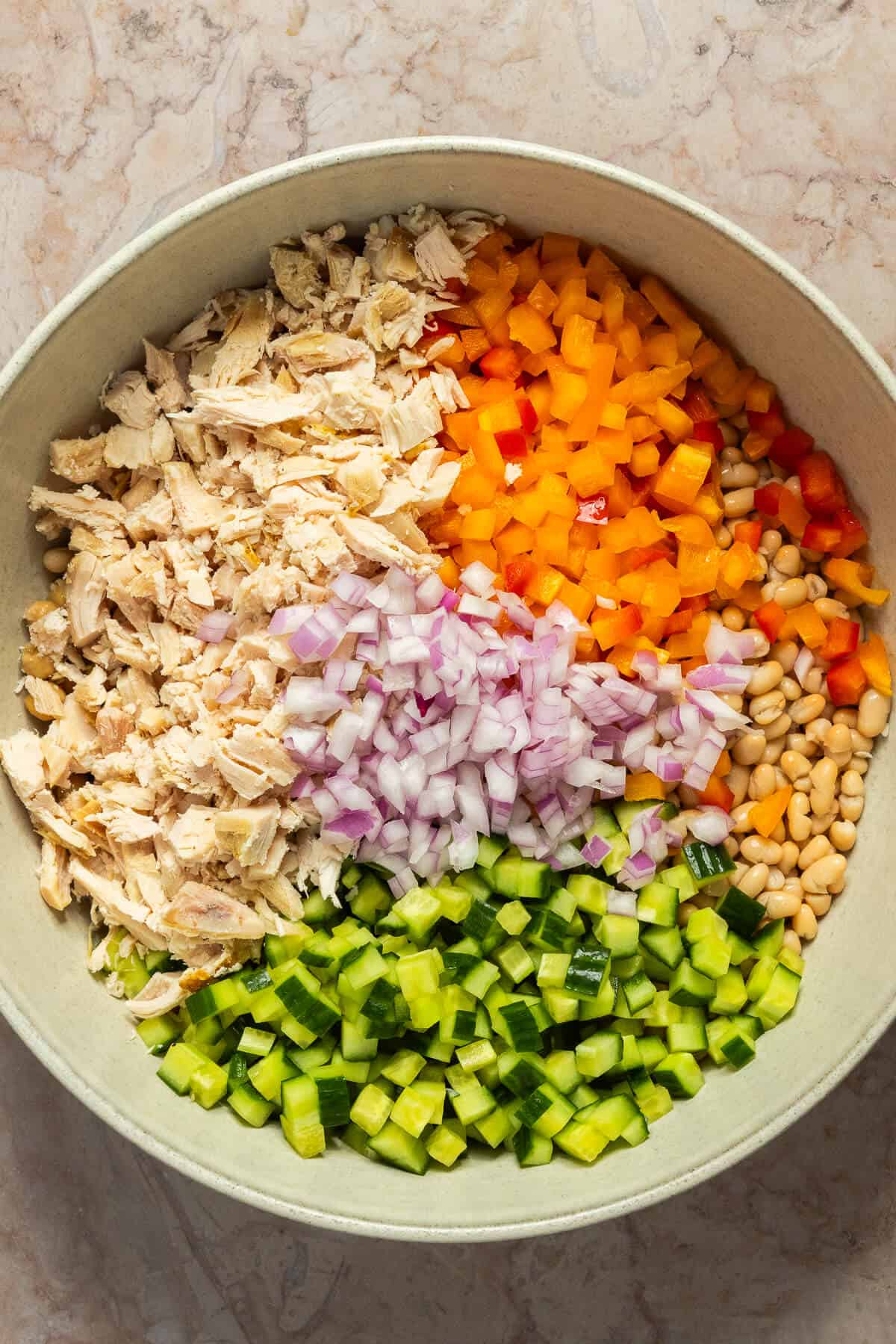 A large mixing bowl with beans, chopped veggies, and chopped chicken prior to mixing.
