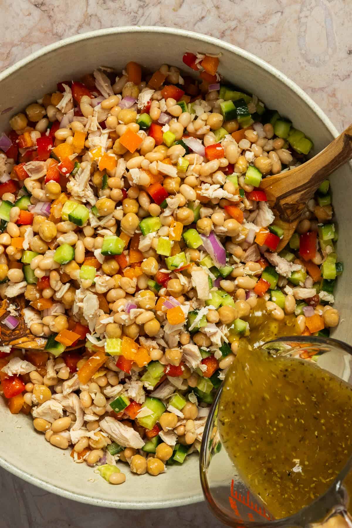 A large mixing bowl with the dressing being poured onto the white bean salad.