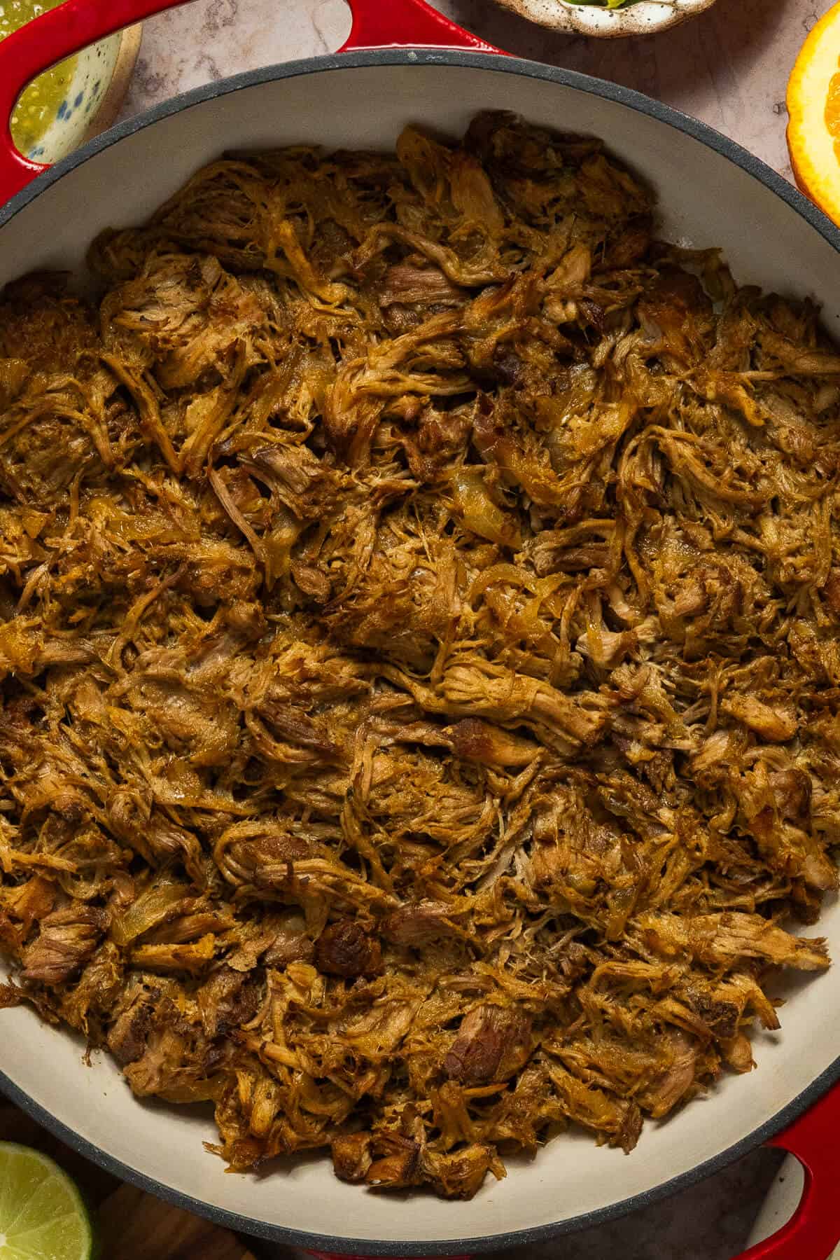Shredded slow cooker pork carnitas in a large pot.