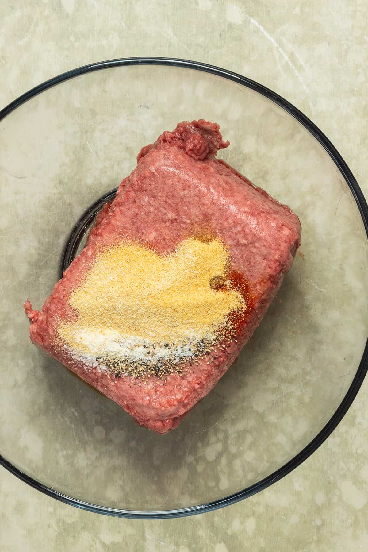 A large mixing bowl with ground beef and seasonings prior to mixing together.