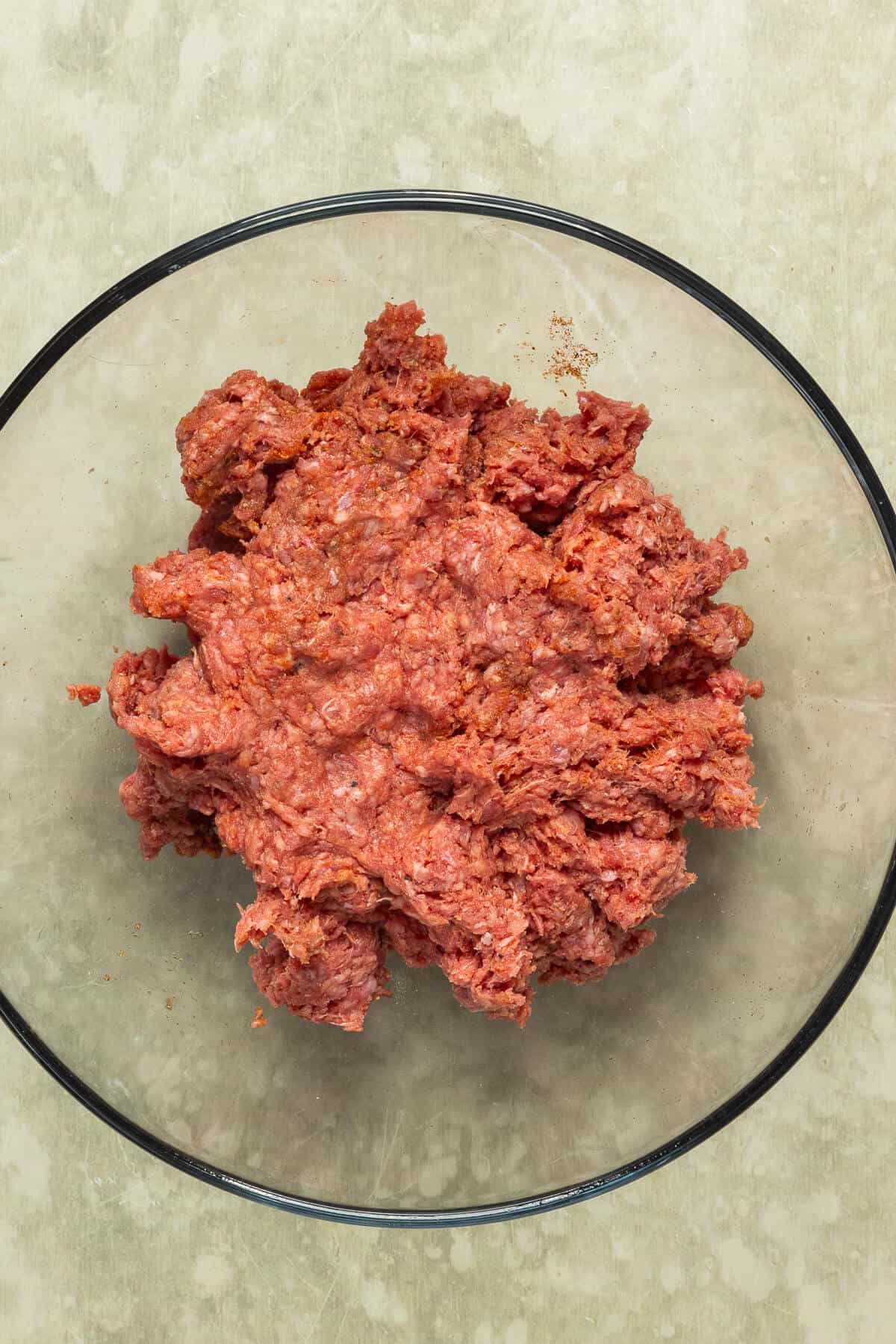 A large mixing bowl with seasoned ground beef prior to cooking.