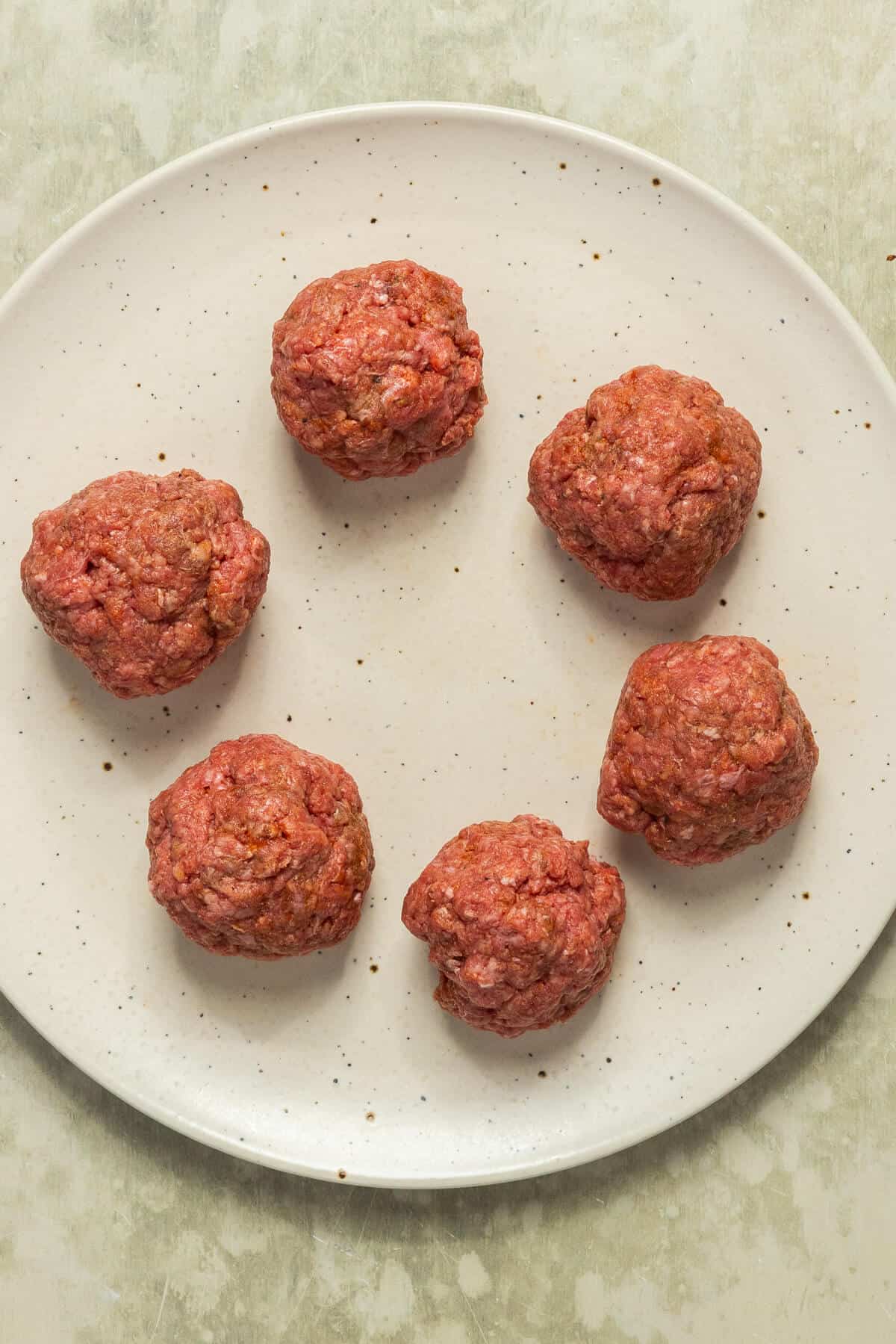 A plate with six balls made of seasoned ground beef.