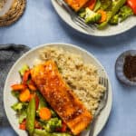 Two plates with brown rice, teriyaki salmon, and roasted vegetables.