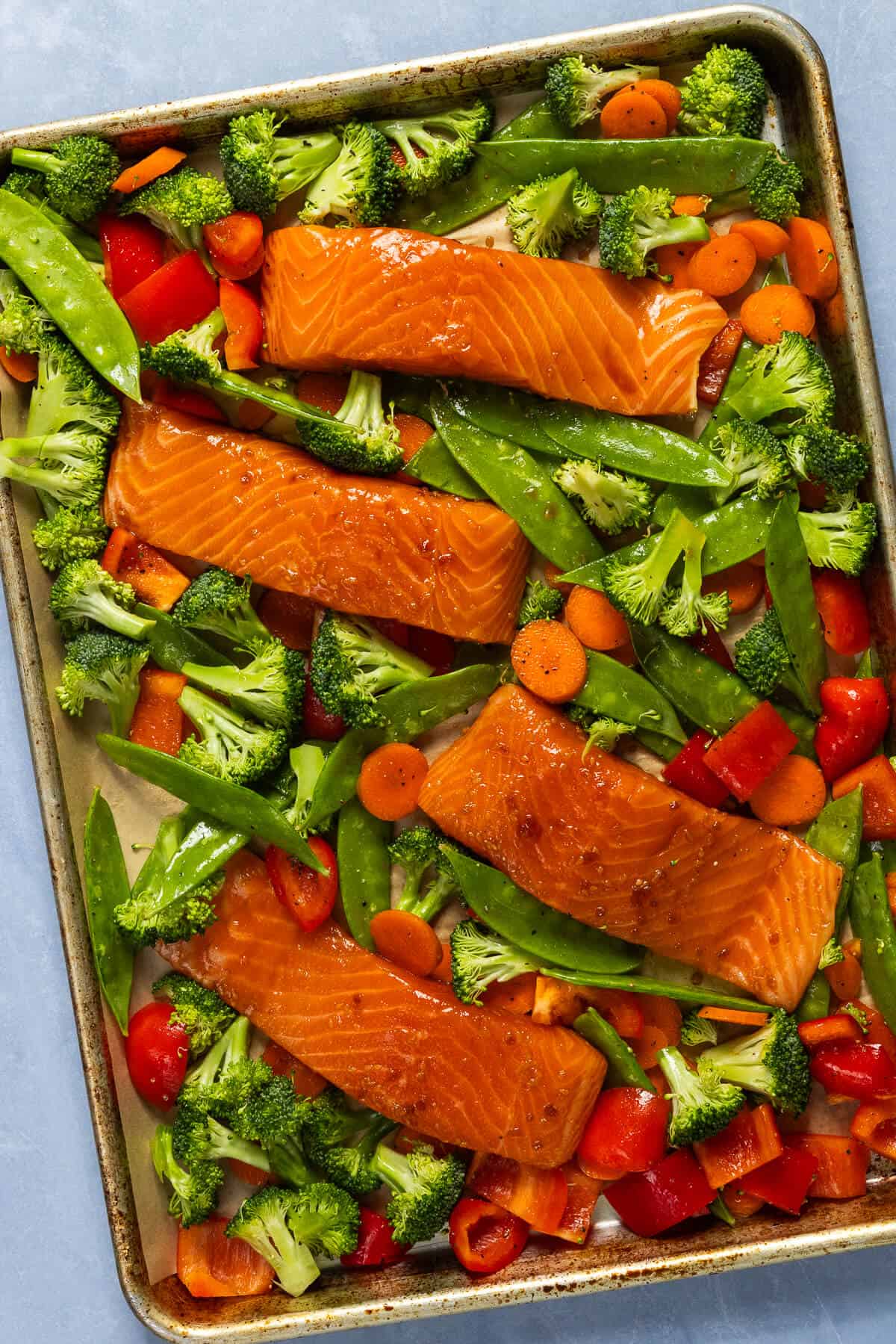 A prepared baking sheet with teriyaki salmon and vegetables prior to baking.
