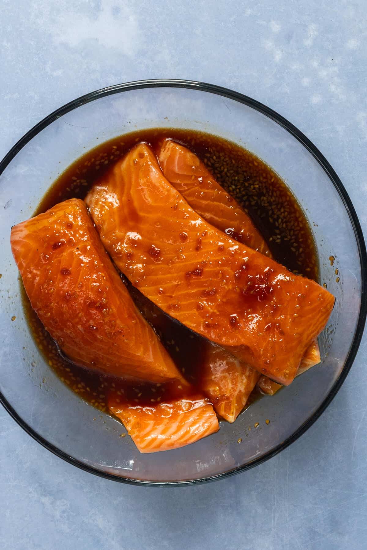 A large bowl with salmon fillets marinating in teriyaki sauce.