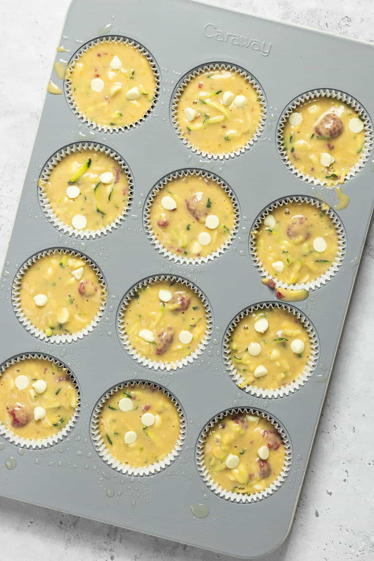 A muffin tin with muffin liners filled with white chocolate raspberry zucchini muffin batter.
