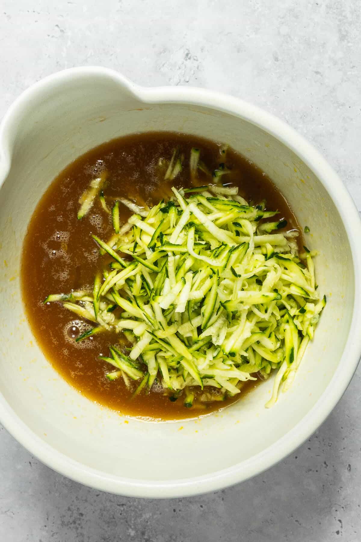 Shredded zucchini added to the large mixing bowl of liquid ingredients.