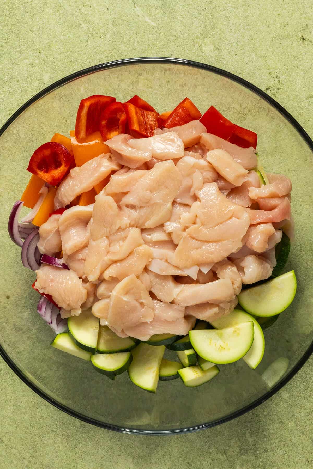 A mixing bowl with cubed chicken and chopped vegetables.