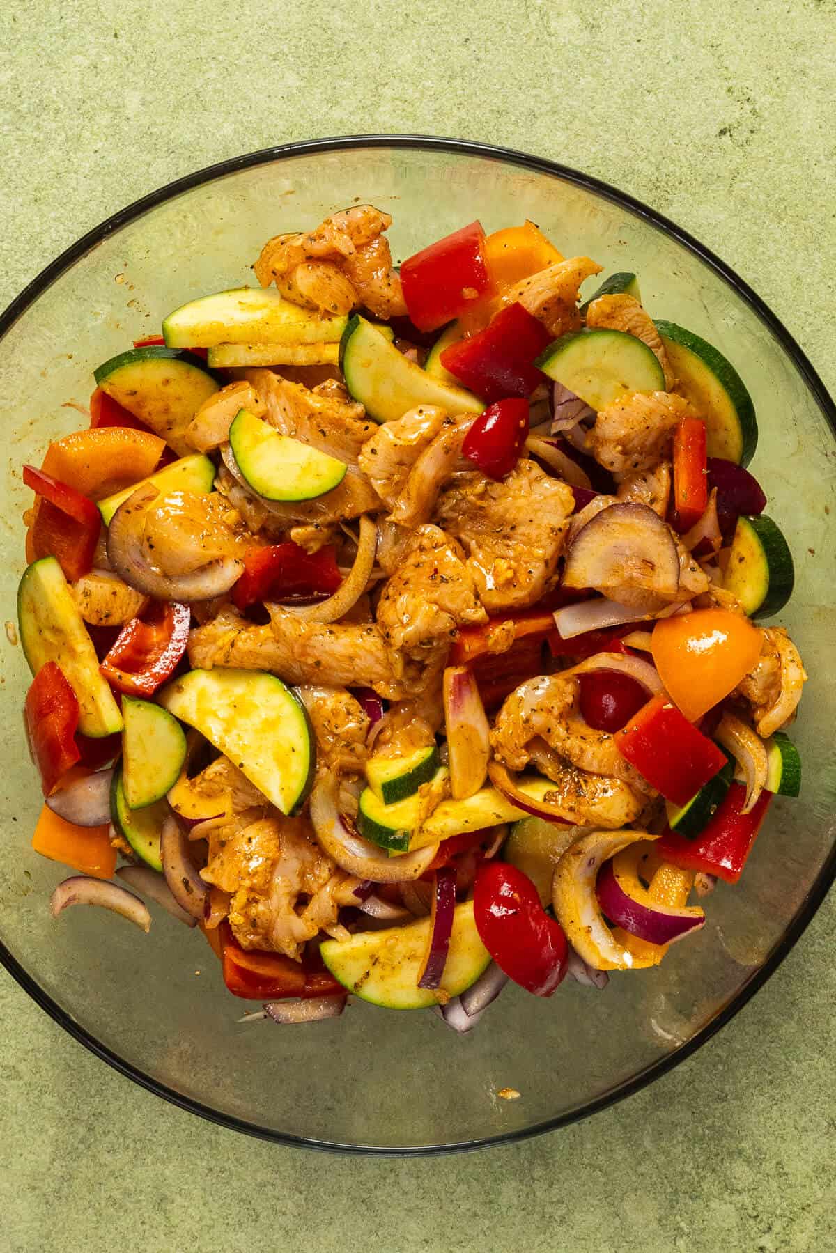 A large mixing bowl with the seasoned chicken and vegetables prior to cooking.