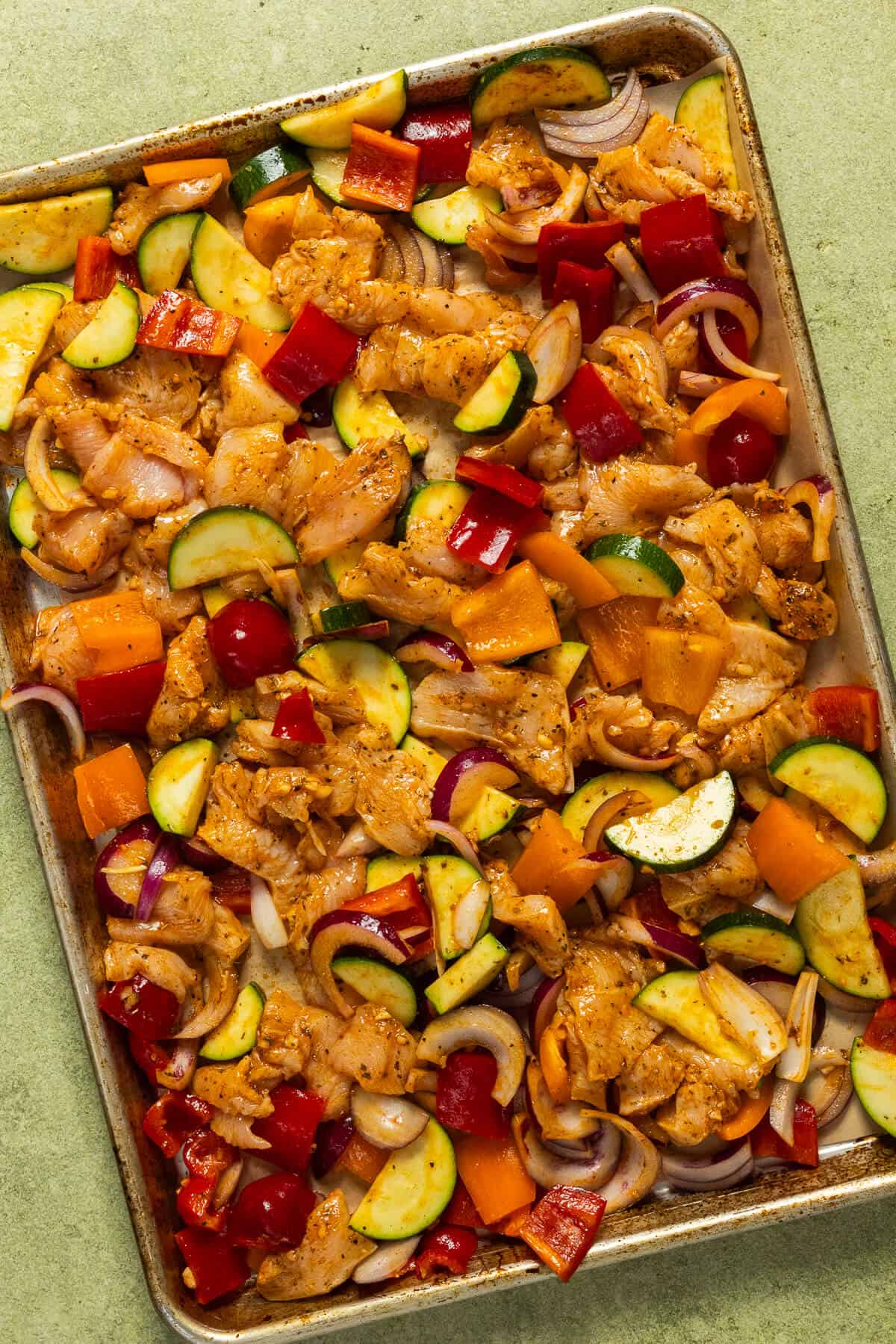 A baking sheet with the chicken and vegetables prior to baking.