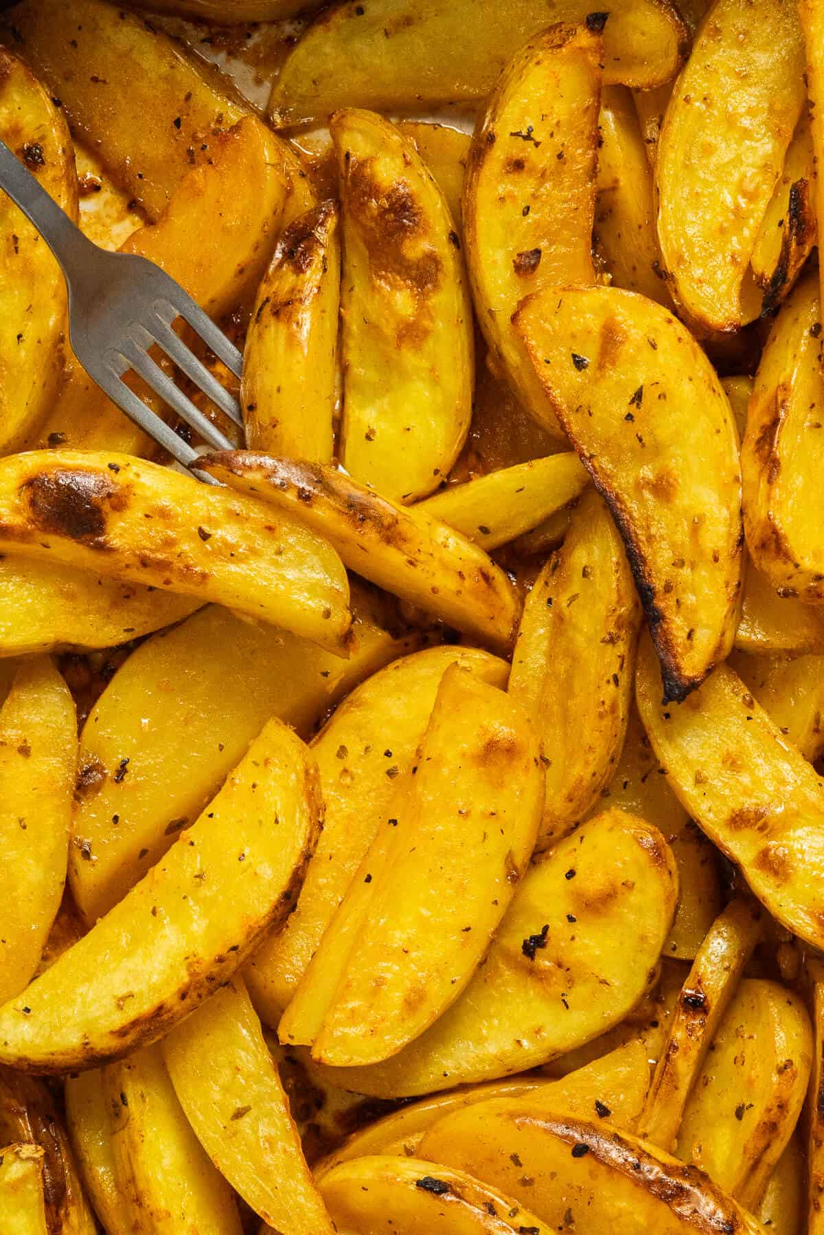 Lemon roasted potato wedges pierced by a fork.