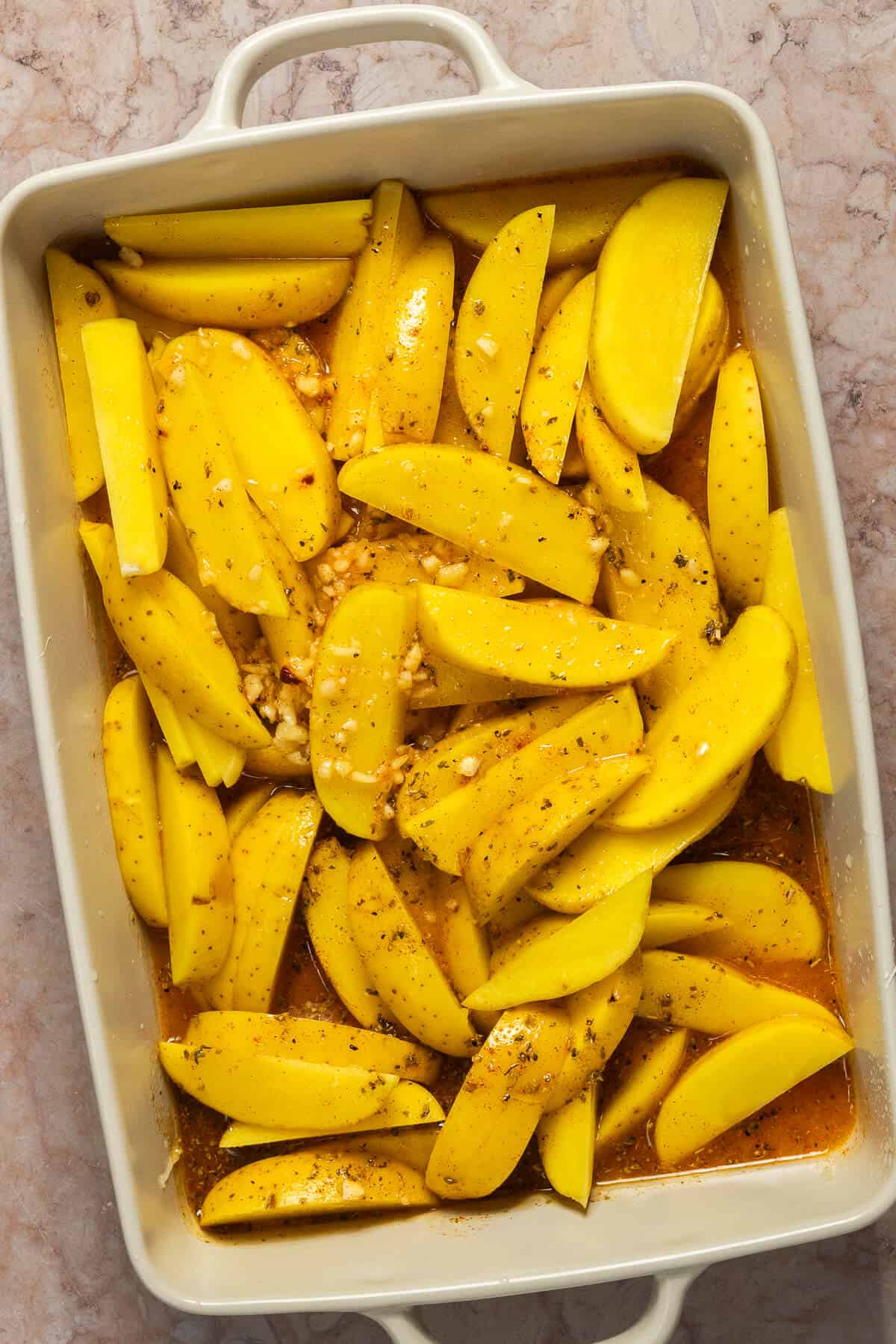 A 9x13 baking dish with potato wedges and the seasonings.