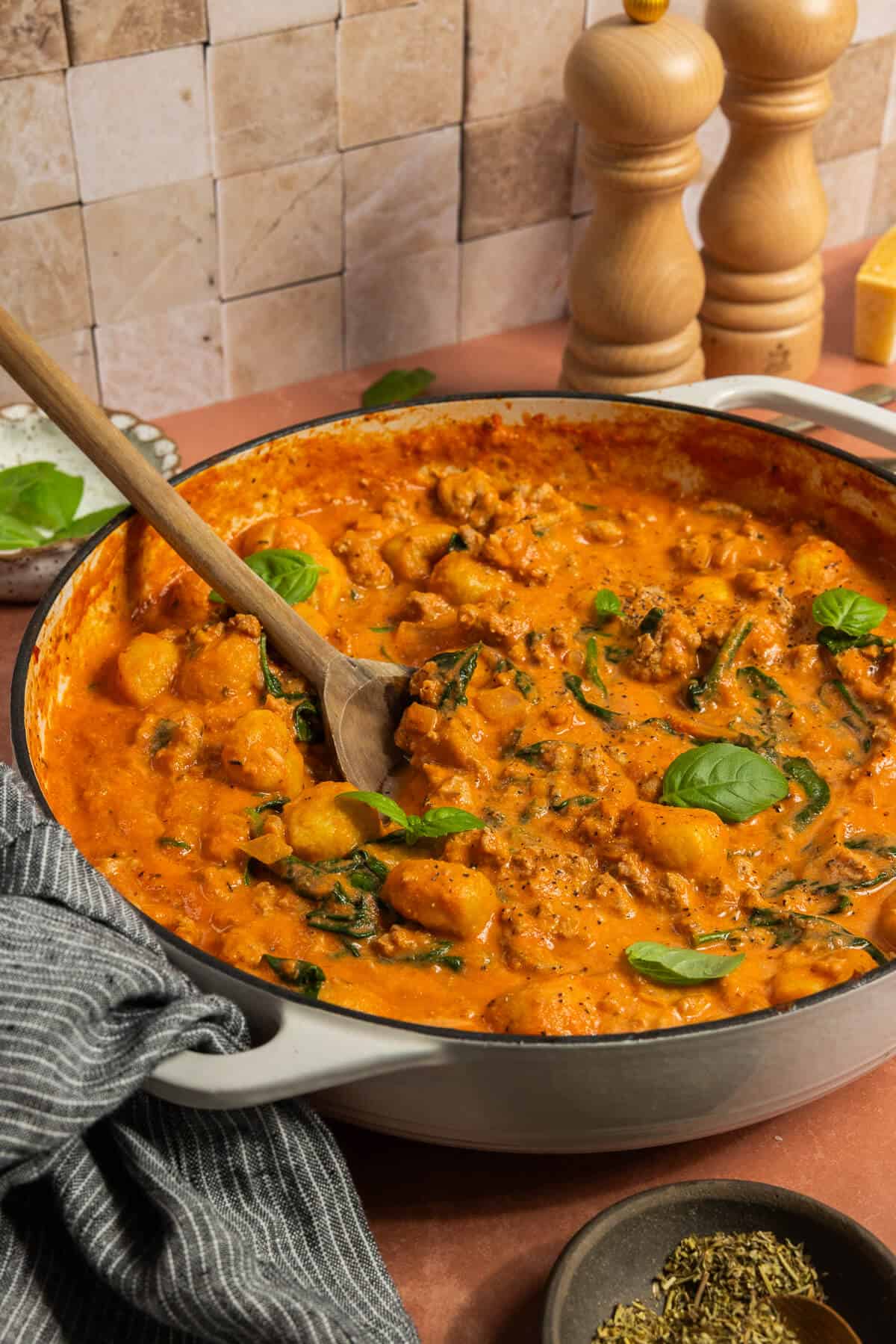 A large skillet and wooden spoon with one pan gnocchi with chicken sausage.