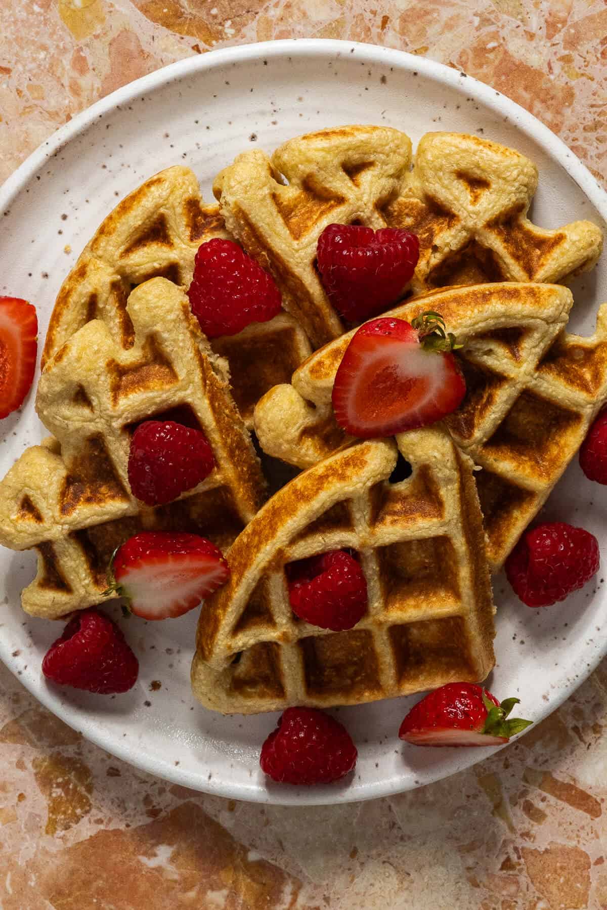 Waffles stacked on a plate with berries.