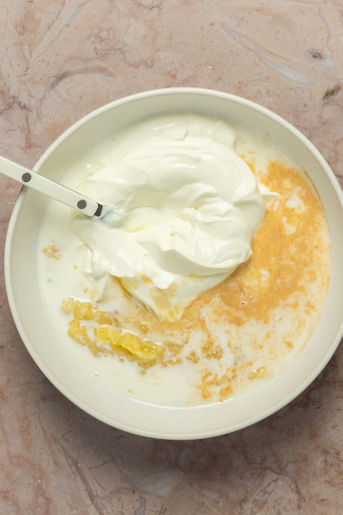 A mixing bowl with mashed banana, Greek yogurt, milk, maple syrup, and vanilla.