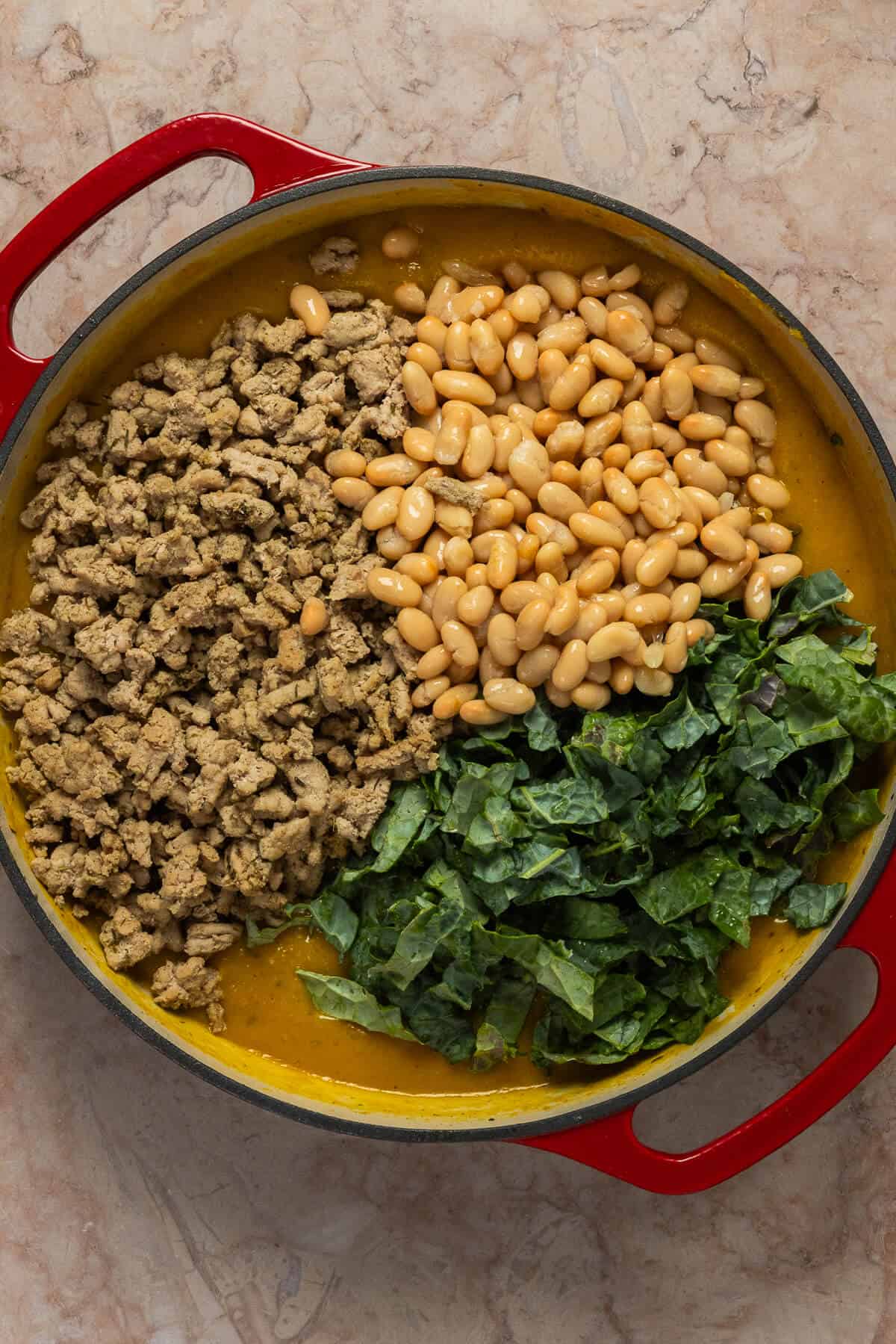 Chopped kale, white beans, and ground meat being added to the butternut squash sauce.