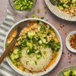 A curry bowl plated with chopped cucumber, green onion, cilantro and red pepper flakes.