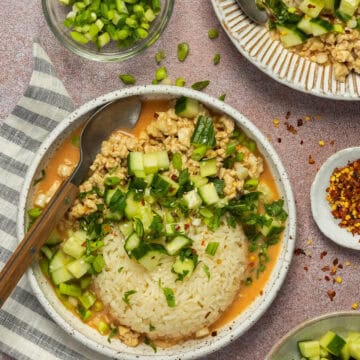 A curry bowl plated with chopped cucumber, green onion, cilantro and red pepper flakes.