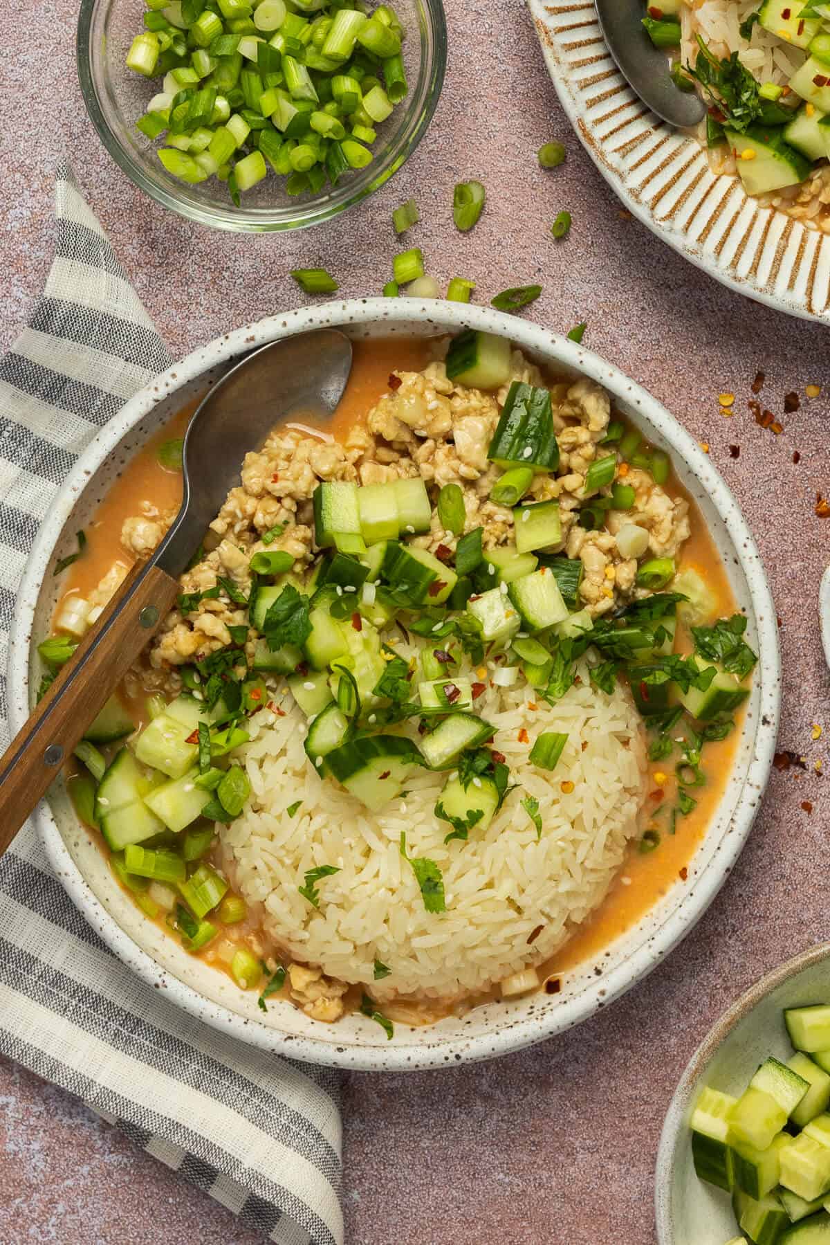 A curry bowl plated with chopped cucumber, green onion, cilantro and red pepper flakes.