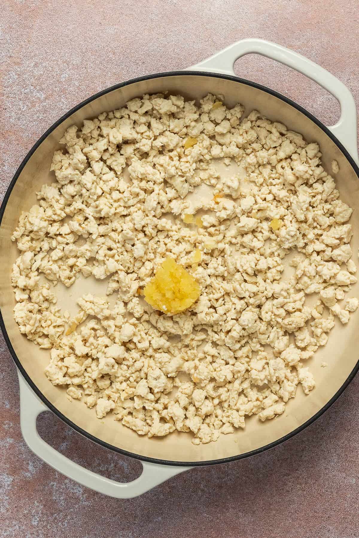 A large skillet with cooked ground chicken and minced garlic.