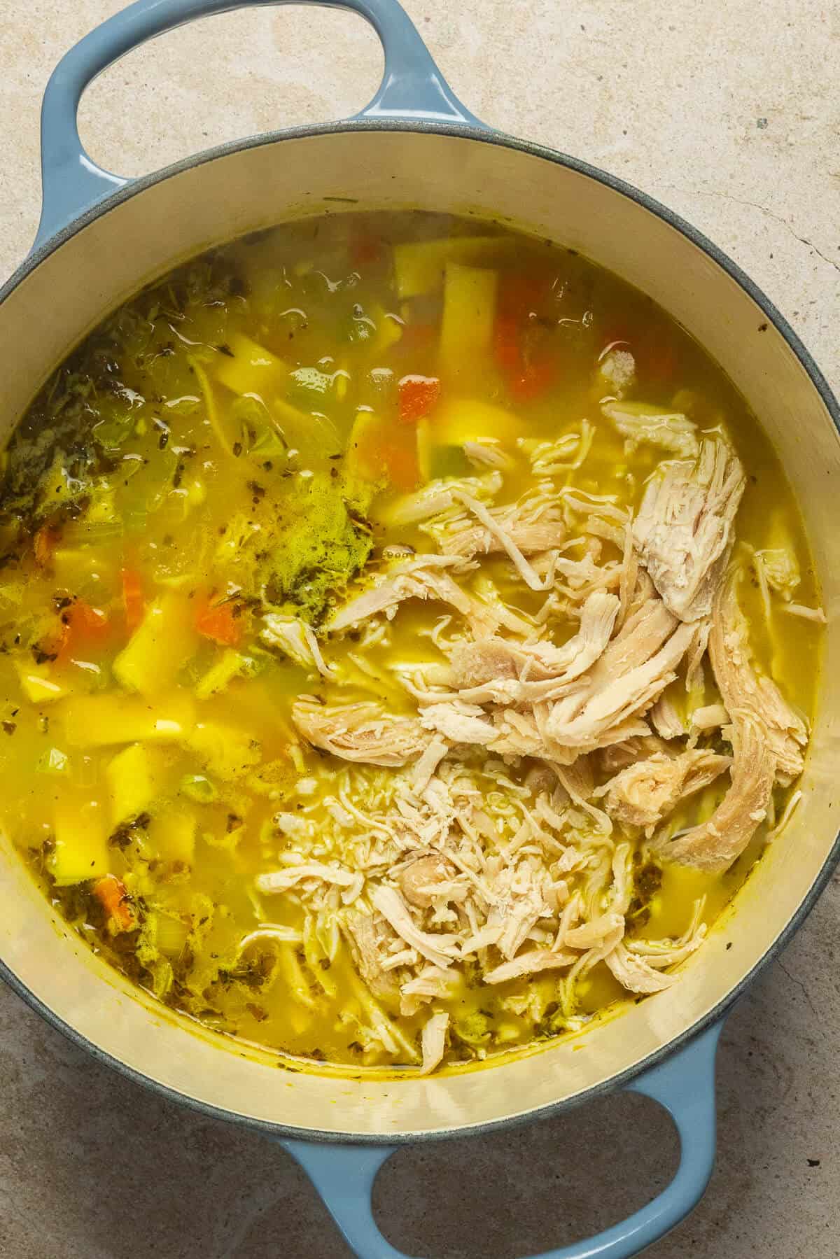 Shredded chicken added to the large pot of chicken noodle soup.