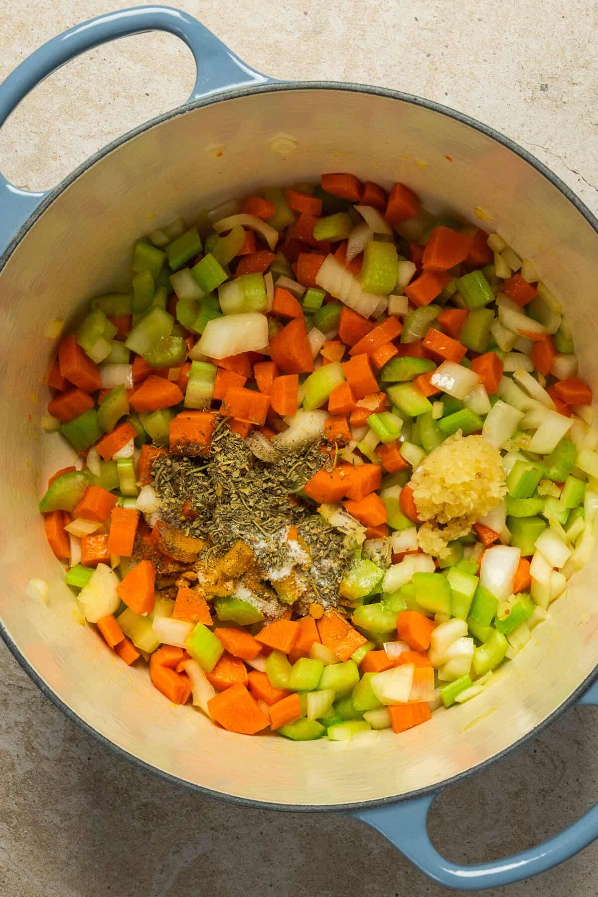 A large pot with diced onion, carrot, and celery and minced garlic and the seasonings for chicken noodle soup.