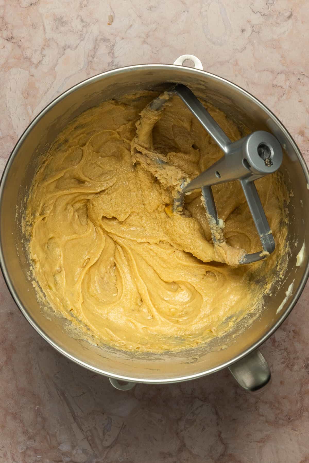A Kitchenaid mixing bowl and paddle mixer with the combined wet ingredients of the cookie dough.