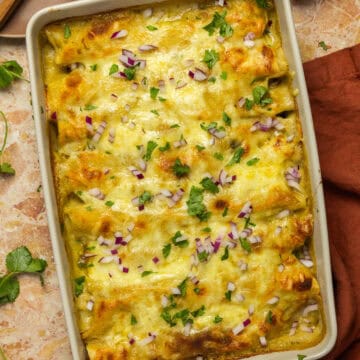 A baking dish with cooked creamy chicken enchiladas with cilantro and red onion.
