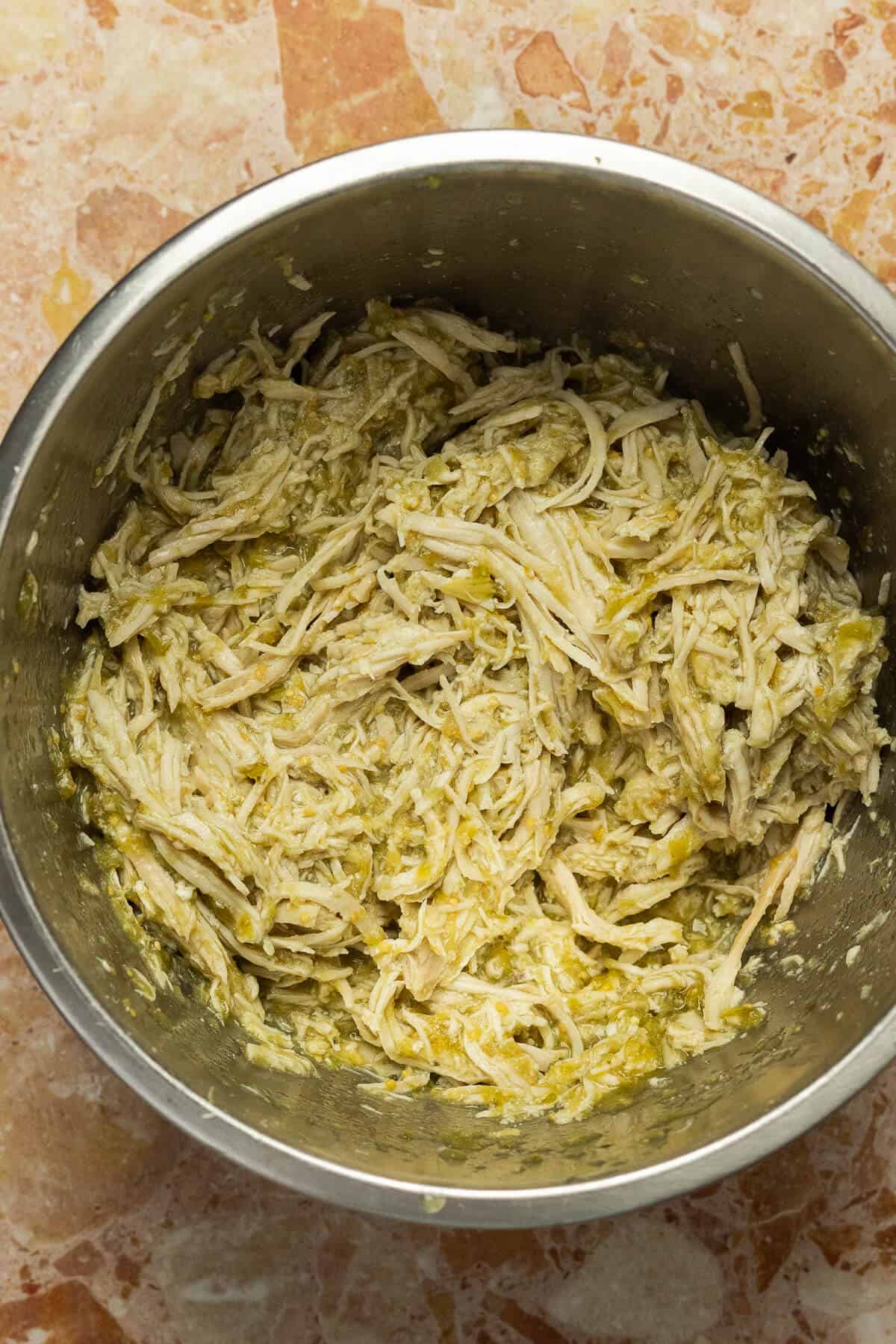 A large mixing bowl with shredded chicken and salsa verde.