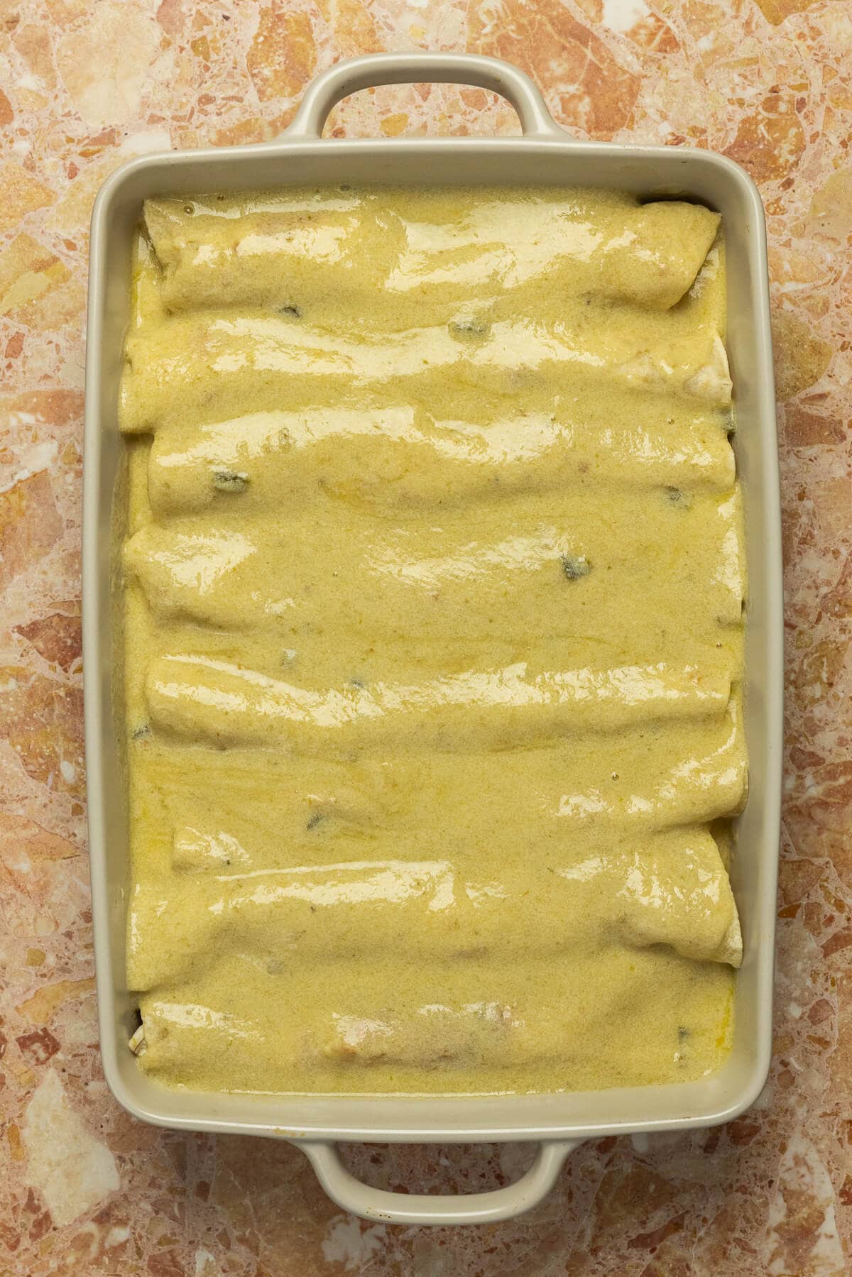 A baking dish with creamy green enchilada sauce added over 8 rolled enchiladas.